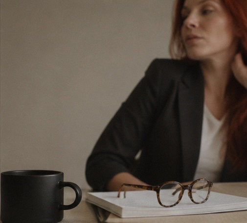 Lindsay seated at a desk with a notebook, glasses, and coffee
